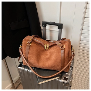 Sac Boston en daim marron avec détails dorés posé sur une valise argentée