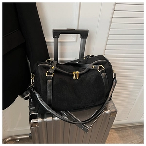 Détail du sac de voyage noir en daim avec fermetures dorées posé sur une valise argentée