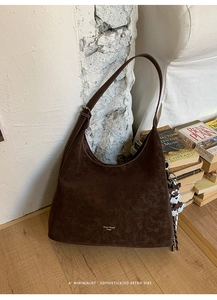 Close-up of retro brown suede hobo bag with a cute puppy charm on a wooden table