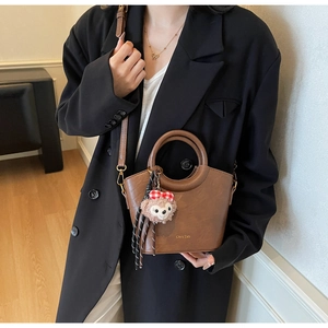 Détail du sac seau en cuir marron avec un pendentif d'ours et un logo doré