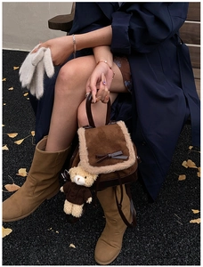 Brown suede backpack with plush trim and teddy bear pendant in an autumn outdoor setting