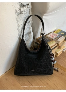 Detail of black suede hobo bag with logo, bear charm and tassels against retro books