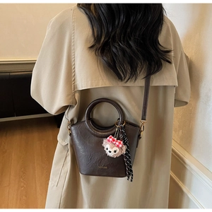 Détail d'un sac seau en cuir PU marron avec charme en peluche et foulard rayé sur un trench-coat