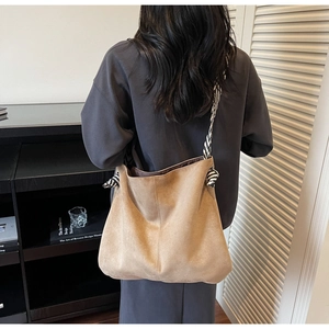 Detail of khaki suede tote bag featuring black and white striped woven rope shoulder strap