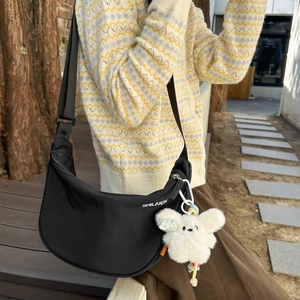 Dettaglio borsa a mezzaluna in nylon nero con logo bianco e ciondolo di peluche