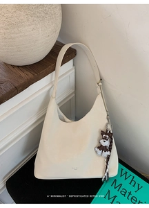 Detail of minimalist cream hobo bag featuring brand logo and cute dog charm on leather strap
