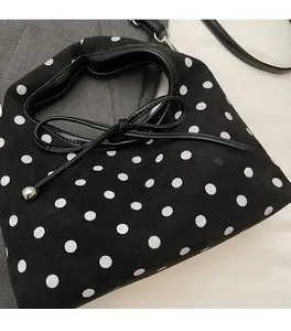 Détail du sac à main noir à pois avec texture suédée et nœud à breloques en métal