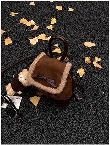 Close-up of brown suede mini backpack with fur trim and plush bear charm on autumn leaves