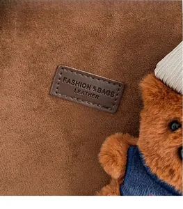 Detail of brown suede tote with leather logo tag and a small teddy bear charm