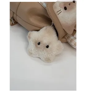 Close-up of a plush star charm in beige faux fur attached to a stylish backpack