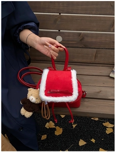 Detail view of red leather backpack with white plush trim and cute bear charm outdoors
