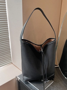 Minimalist black suede tote bag with leather trim and drawstring detail on a display shelf