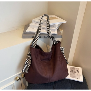 Detail of dark brown suede tote bag with striped woven strap and artistic background