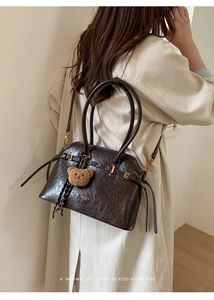 Détail d'un sac à main marron foncé effet cuir craquelé avec charm ours en peluche