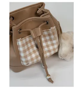 Detail of brown bucket bag with plaid pocket, drawstring closure and plush pendant