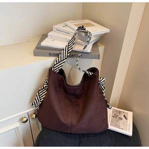 Detail of dark brown suede tote bag featuring a black and white woven strap and bow knot