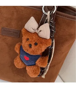 Close-up of a brown plush bear charm with heart embroidery on a suede tote bag