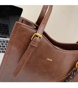Close-up of vintage brown leather tote bag with gold logo and premium metal buckles