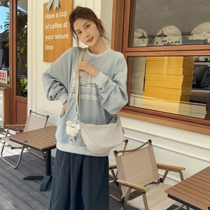 Dettaglio di una borsa a tracolla bianca in nylon con ciondolo peluche su una felpa azzurra