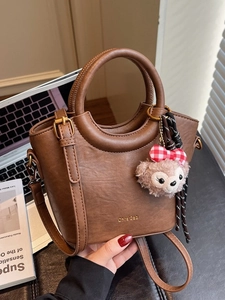 Sac seau marron en cuir avec poignée et breloque en peluche dans un décor de bureau