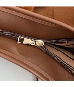 Close-up of a polished gold zipper pull on a brown leather tote bag with striped lining