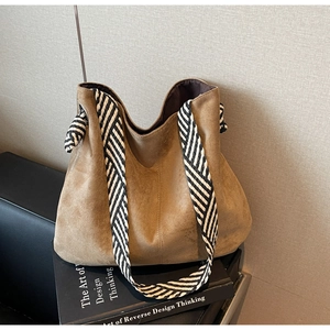 Detail of brown suede tote bag featuring a stylish black and white woven shoulder strap