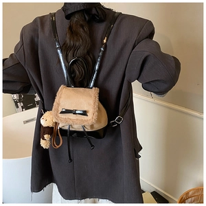 Detail of a brown suede backpack with fuzzy trim and a teddy bear charm on grey blazer