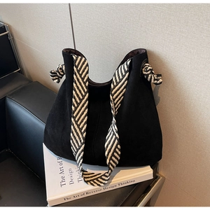 Detail of black suede tote bag with striped woven strap on a modern armchair