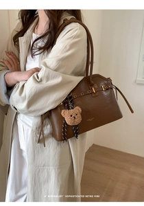 Détail du sac à main en cuir marron avec œillets dorés et breloque ours en peluche amovible