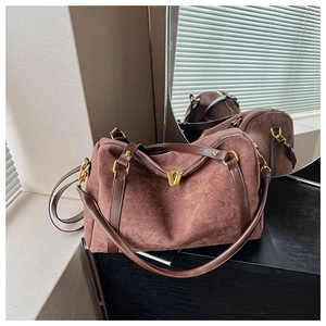 Détail d'un sac Boston en daim marron avec ferrures dorées sur une table en bois noir