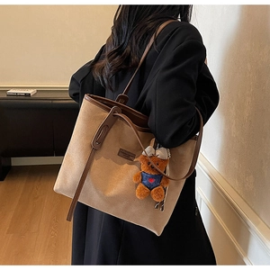 Detailed view of brown suede tote bag featuring a cute teddy bear charm on shoulder strap