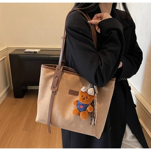 Close-up of brown suede tote bag featuring a leather logo patch and cute bear keychain