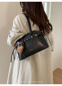 Détail du sac cabas noir brillant avec texture froissée, boucle dorée et breloque