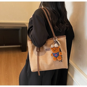 Detail of brown matte tote bag with leather straps and cute plush bear accessory
