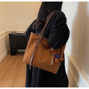 Detail of brown suede tote bag with cute bear charm worn on a black wool coat