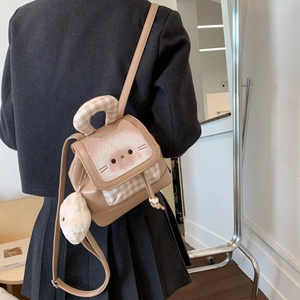 Detail of khaki leather cat backpack featuring cute facial embroidery and a plush ball charm