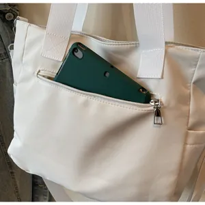 Gros plan d'un cabas en nylon crème montrant une poche zippée avec un téléphone mobile