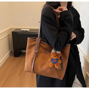 Detail of warm brown suede tote bag with leather logo patch and cute plush bear charm