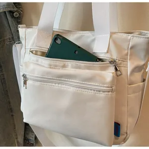 Gros plan d'une tablette glissée dans la poche zippée avant du grand sac fourre-tout blanc
