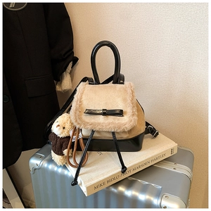 Detail of mini black leather backpack featuring beige faux fur flap and bow decoration