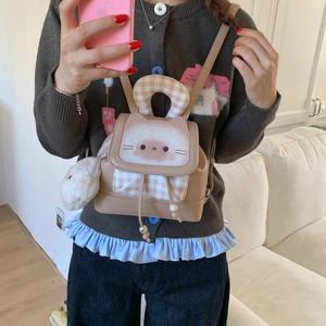 Close-up of beige mini backpack with cat print, plaid pocket, and plush ball charm