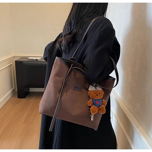 Detail of dark brown matte tote bag with cute bear charm worn by a model in black blazer
