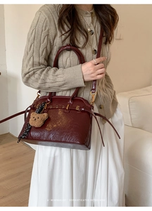 Détail du sac à main vintage en cuir bordeaux avec breloque ours et boucles dorées