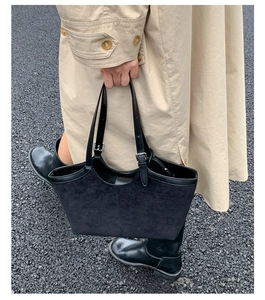 Detail of black suede tote bag featuring adjustable leather handle and metal buckle