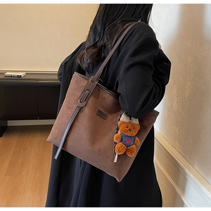 Detail of dark brown suede tote bag featuring a cute plush bear charm on the strap
