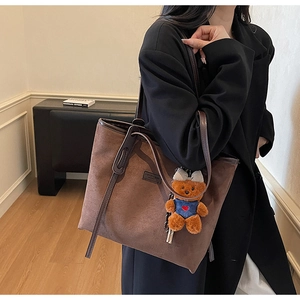 Close-up of brown suede tote bag featuring leather handle and a cute plush bear charm
