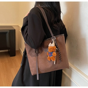 Close-up of brown matte suede tote bag featuring a cute plush bear charm on the shoulder strap