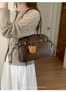 Détail du sac à main en cuir marron foncé avec boucle dorée et pendentif ours