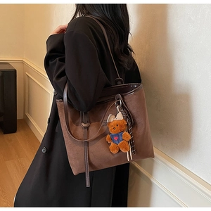 Detail of large brown suede tote bag with slim handles and a cute bear plush charm