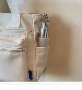 Détail de la poche latérale ouverte avec boucles métalliques sur un sac fourre-tout crème